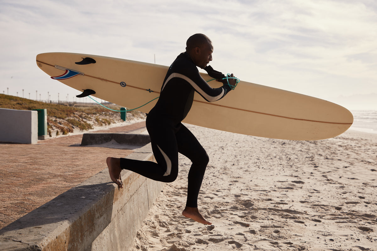 man with surfboard sprinting on the sand